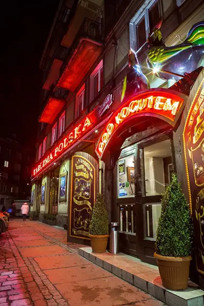 Wejście do karczmy nocą, nad nim czerwony neon Karczma Polska